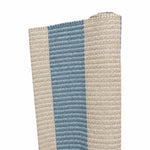 A close-up of the Magdalena York Amy Stripe in Medium Blue rug, showcasing its artisanal beige and blue vertical stripes, partially rolled up against a white background.
