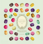 An assortment of vibrant macarons is elegantly arranged in a circle around the cover of Simon & Schuster’s Ladurée Macarons, which features a decorative central emblem, showcasing the artistry behind crafting exquisite ganache-filled delights.