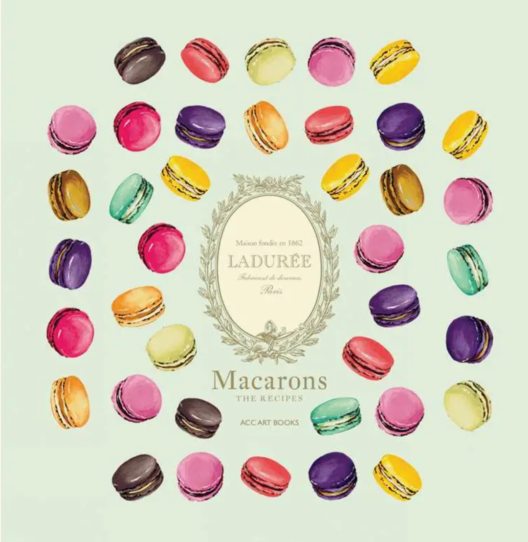 An assortment of vibrant macarons is elegantly arranged in a circle around the cover of Simon & Schuster’s Ladurée Macarons, which features a decorative central emblem, showcasing the artistry behind crafting exquisite ganache-filled delights.