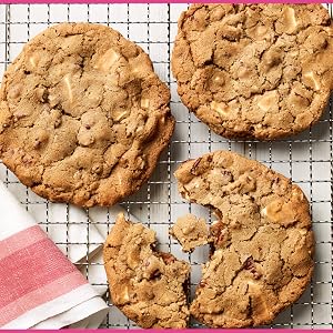 Three large cookies, inspired by Martha Stewart’s Cookie Perfection from Penguin Random House—one broken in half—rest on a wire cooling rack beside a red and white striped napkin.