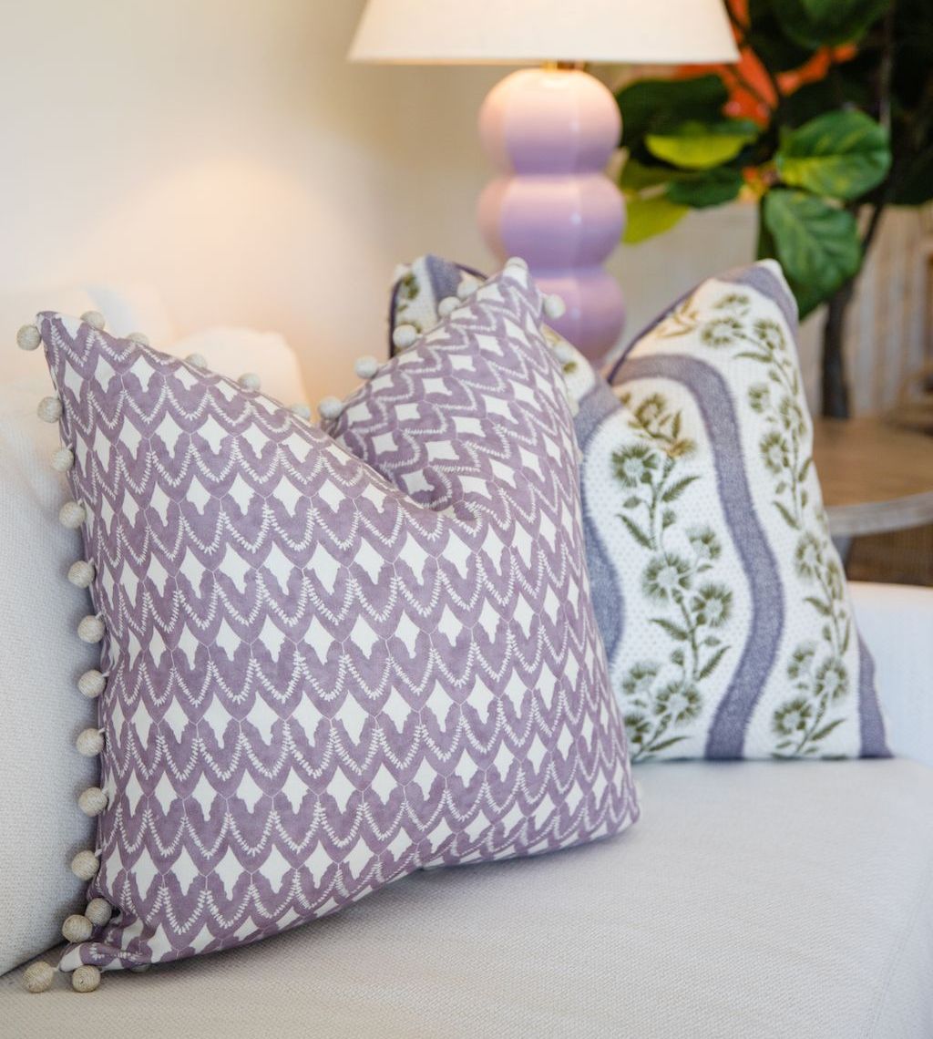 Two Harwick Stripe Olive and Plum Pillows by Hive Custom Pillows rest on a light-colored sofa, with a lamp and leafy plant visible in the background.