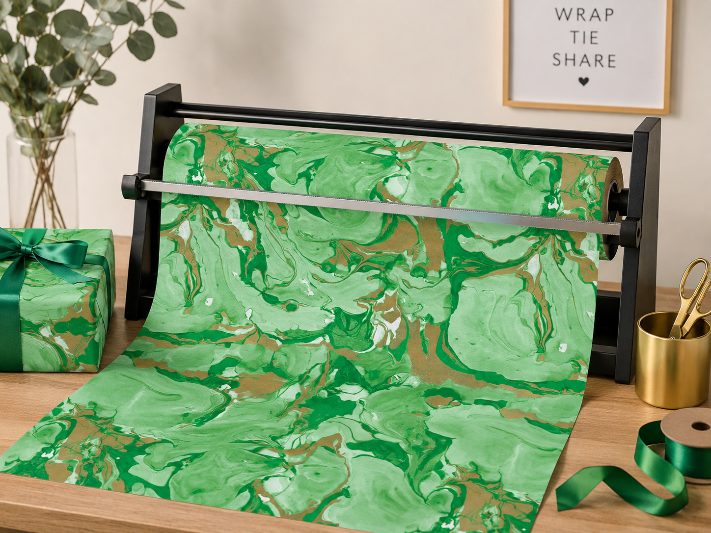 A roll of Caspari Marbled Green Roll Wrap made from heavyweight paper sits on a dispenser atop a wooden table, surrounded by gift wrapping supplies and a framed sign in the background. Printed with earth-friendly inks, this Caspari wrap is perfect for thoughtful and sustainable presentations.