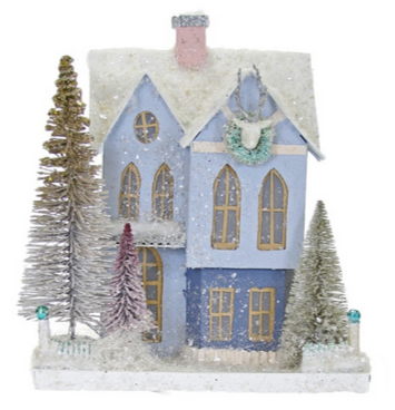 The Cody Foster Purple Frosted Mansionette, measuring 8"L x 8.25"W x 16"H, features a blue house design with a frosted roof and small snow-covered trees, adorned with a wreath and deer’s head above the door.