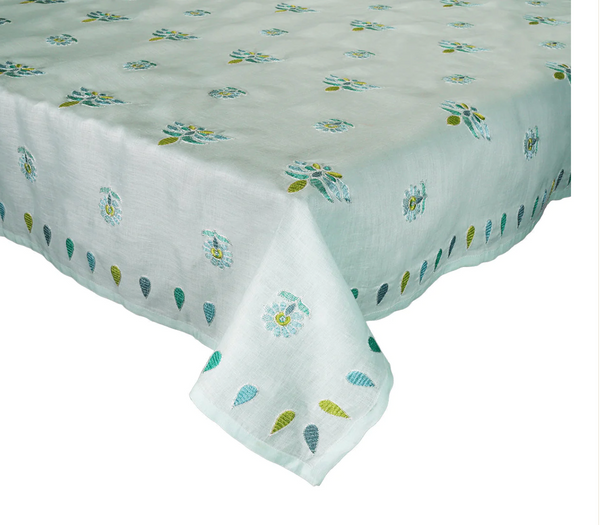 A Kim Seybert Lima Seafoam Tablecloth, beautifully designed with a pattern of small blue and green flowers and leaves, gracefully decorates the dining table.