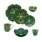 The Green Cabbage Dinnerware Collection by Bordallo Pinheiro features plates, bowls, a mug, and small dishes, crafted in Portugal and shaped like cabbage leaves.