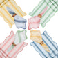 Four napkin sets from Juliska’s Cabana Stripe Tabletop Collection in yellow, green, red, and blue are arranged in a circle, each accented by a complementary fold and wooden ring.
