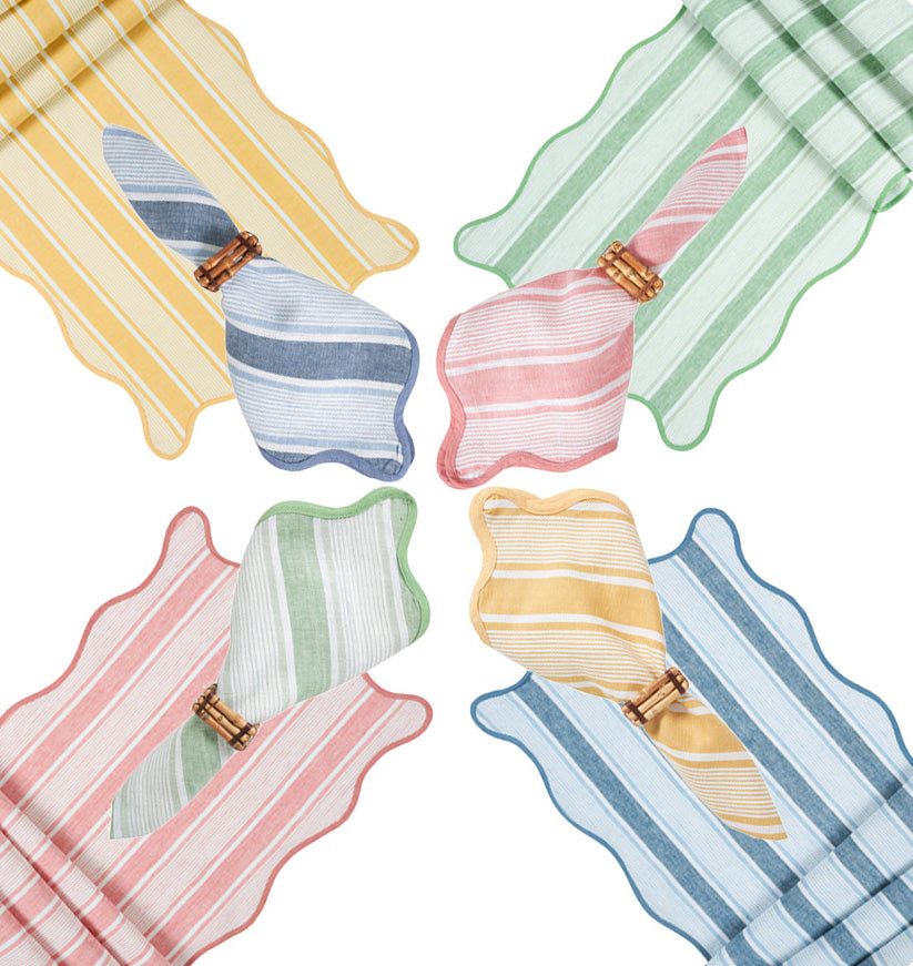 Four napkin sets from Juliska’s Cabana Stripe Tabletop Collection in yellow, green, red, and blue are arranged in a circle, each accented by a complementary fold and wooden ring.