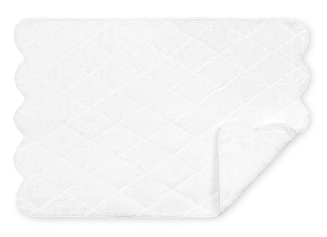 The Matouk Cairo Scallop Bath Collection features a luxurious white quilted mat crafted from long-staple cotton, with scalloped edges and a slightly folded corner.
