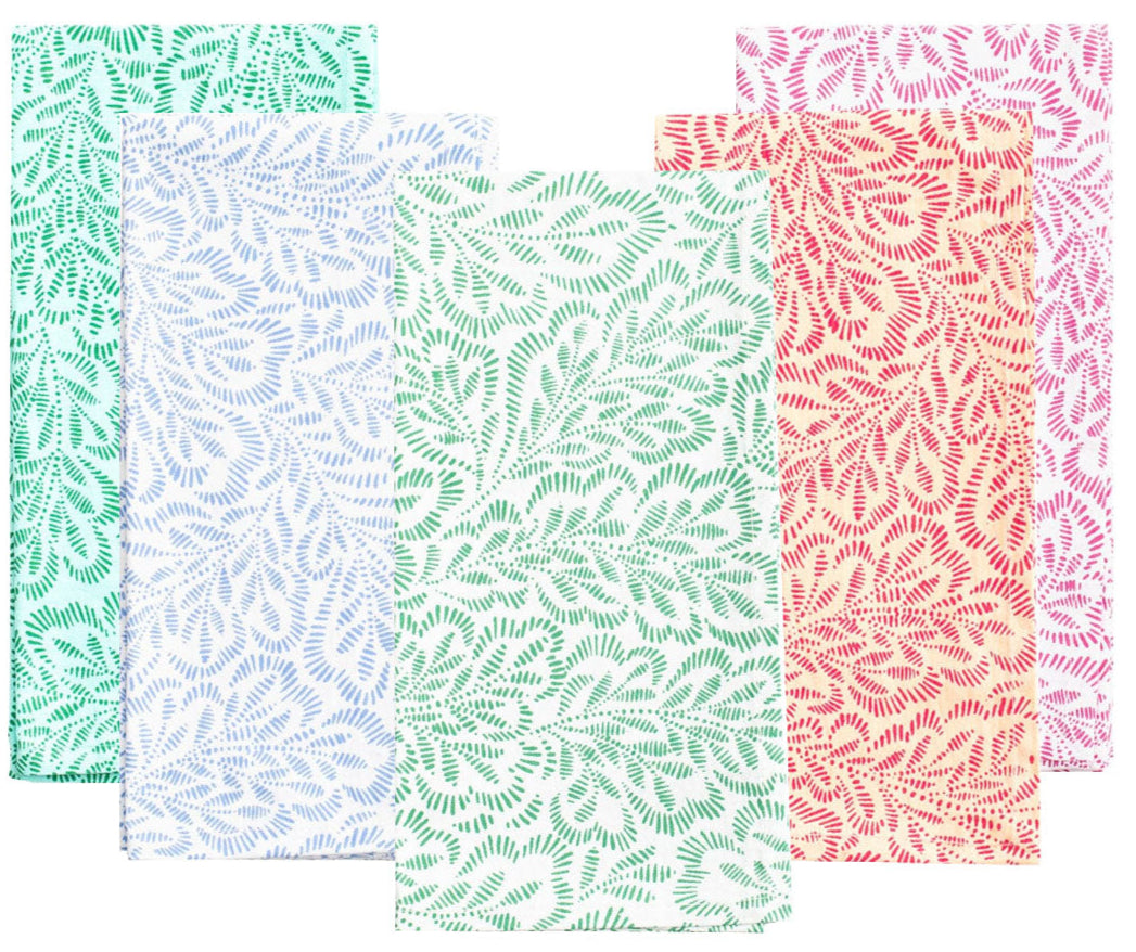 Caspari's Block Print Leaves Napkin Collection features four handcrafted cotton napkins with leafy patterns in green, light blue, mint, and coral pink, beautifully highlighting the charm of Indian textiles.