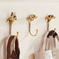 Three Cast Brass Dog Hooks by Rejuvenation, shaped like dog heads, hold a belt, a tote bag, and a leather strap against a white wall.