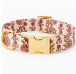 The Foggy Dog Blockprint Floral Dog Collar showcases a pink and gold floral pattern inspired by hand-carved block prints, and features a gold metal buckle and D-ring. The collar is displayed against a white background.