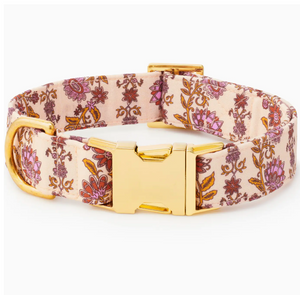 The Foggy Dog Blockprint Floral Dog Collar showcases a pink and gold floral pattern inspired by hand-carved block prints, and features a gold metal buckle and D-ring. The collar is displayed against a white background.
