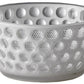 The Lente Acrylic Dinnerware Collection by Mario Luca Giusti features clear glass-look bowls with raised round bumps, ideal for outdoor entertaining or pairing with blue pieces for a vibrant table setting.