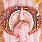 Elegant pink table setting featuring Juliska Cabana Stripe table runner, decorative plate, scalloped napkin, bamboo utensils, juice glass, and a textured charger by Juliska.