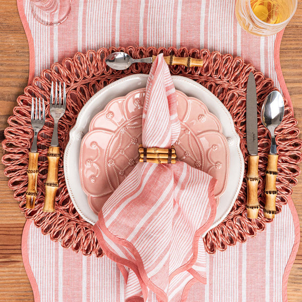 Elegant pink table setting featuring Juliska Cabana Stripe table runner, decorative plate, scalloped napkin, bamboo utensils, juice glass, and a textured charger by Juliska.