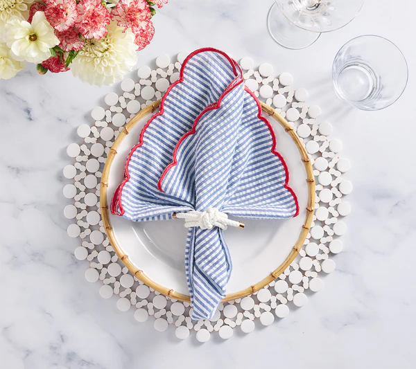A table setting featuring the Kim Seybert Fiesta Napkin Set, a white plate, beaded placemat, white napkin ring, clear glasses, and a floral arrangement.