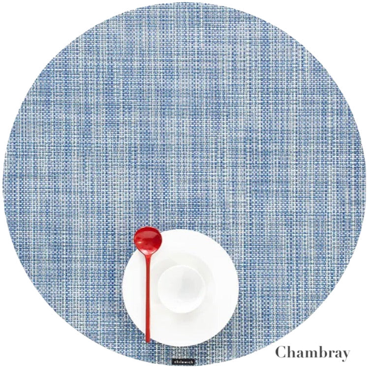 A red spoon rests on a white cup and saucer atop the Chilewich round blue placemat from the Chambray collection, crafted from phthalate-free Terrastrand yarns.