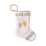 The Champagne Toast Needle Point Stocking by Bauble Stockings features two clinking champagne glasses with green leafy accents, hand-stitched needlepoint, and a gold hanging loop—a festive keepsake ornament.