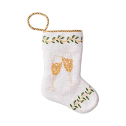 The Champagne Toast Needle Point Stocking by Bauble Stockings features two clinking champagne glasses with green leafy accents, hand-stitched needlepoint, and a gold hanging loop—a festive keepsake ornament.