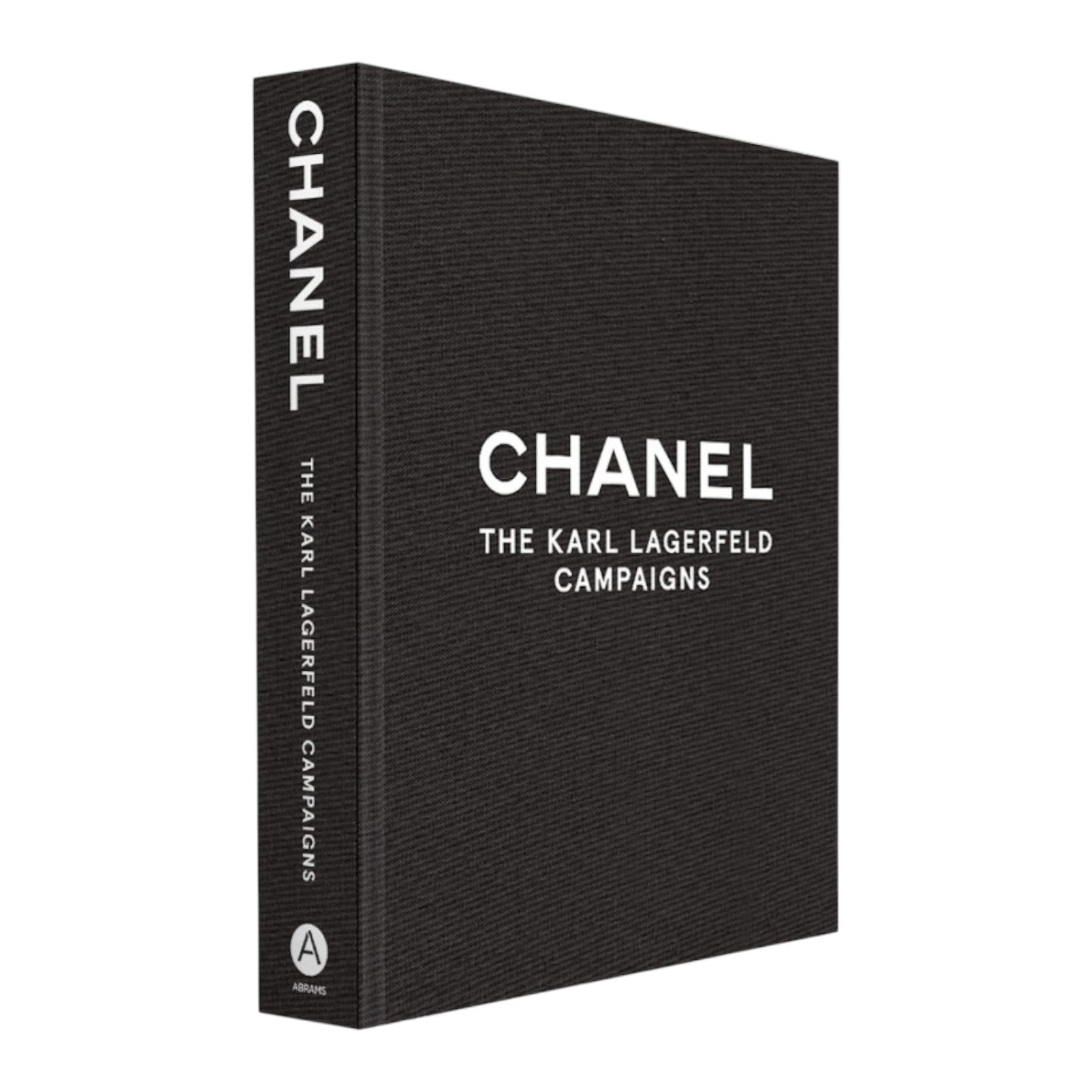A black hardcover coffee table book, "Chanel: The Karl Lagerfeld Campaigns" by Abrams, features striking photography and bold white text on the cover and spine.