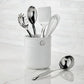 The Hestan Provisions Porcelain Bain Marie, filled with metal kitchen tools like a whisk, spatula, spoon, and pasta server, sits on a marble countertop with a ladle—ideal for organizing your Hestan essentials.