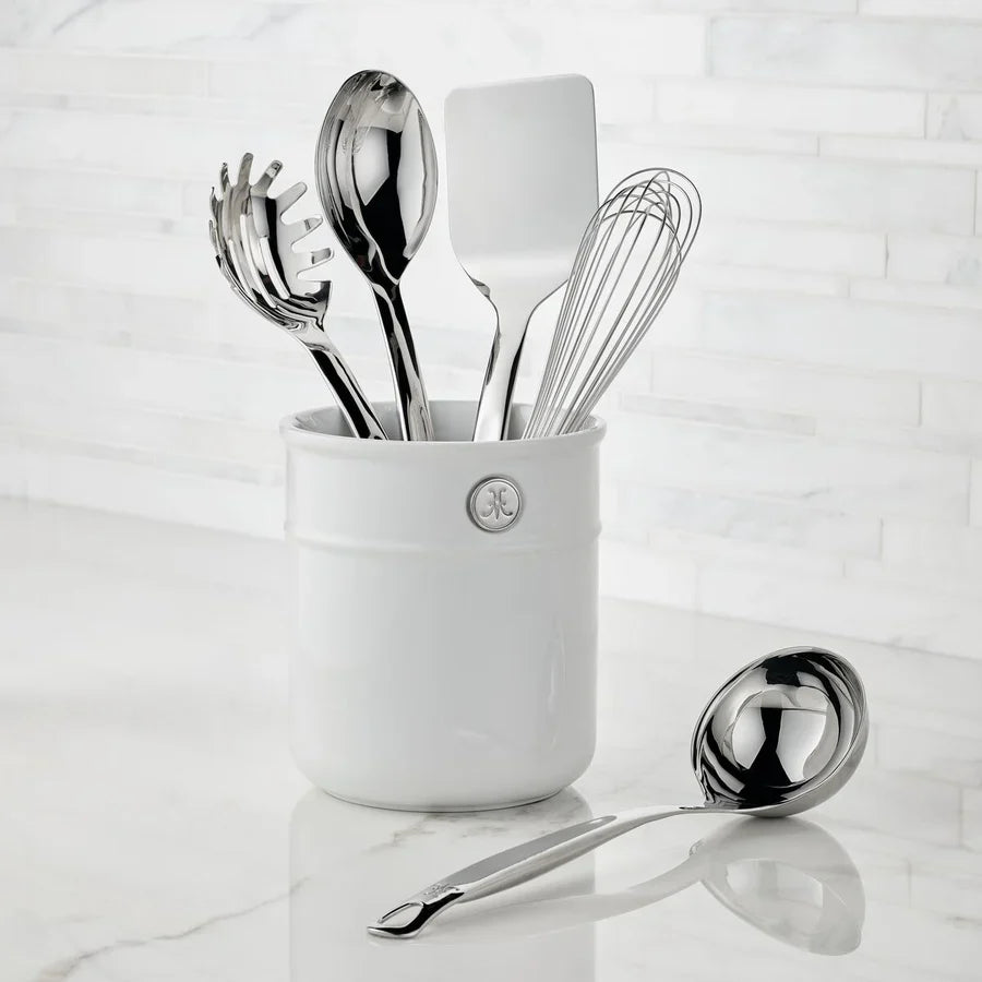 The Hestan Provisions Porcelain Bain Marie, filled with metal kitchen tools like a whisk, spatula, spoon, and pasta server, sits on a marble countertop with a ladle—ideal for organizing your Hestan essentials.