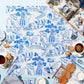 A finished Tart by Taylor Acrylic Puzzle from the Bubbly Butterfly collection, featuring blue and white floral and architectural patterns, is set on a light blue surface with tea, cookies, plates, napkins, and an open book—a charming home decor accent.