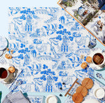 A finished Tart by Taylor Acrylic Puzzle from the Bubbly Butterfly collection, featuring blue and white floral and architectural patterns, is set on a light blue surface with tea, cookies, plates, napkins, and an open book—a charming home decor accent.