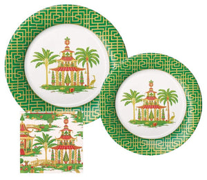 The Caspari Christmas Pagodas Collection includes a salad plate, dinner plate, and matching cocktail napkin, each with a green and gold geometric border featuring a decorative pagoda, palm trees, and cranes.