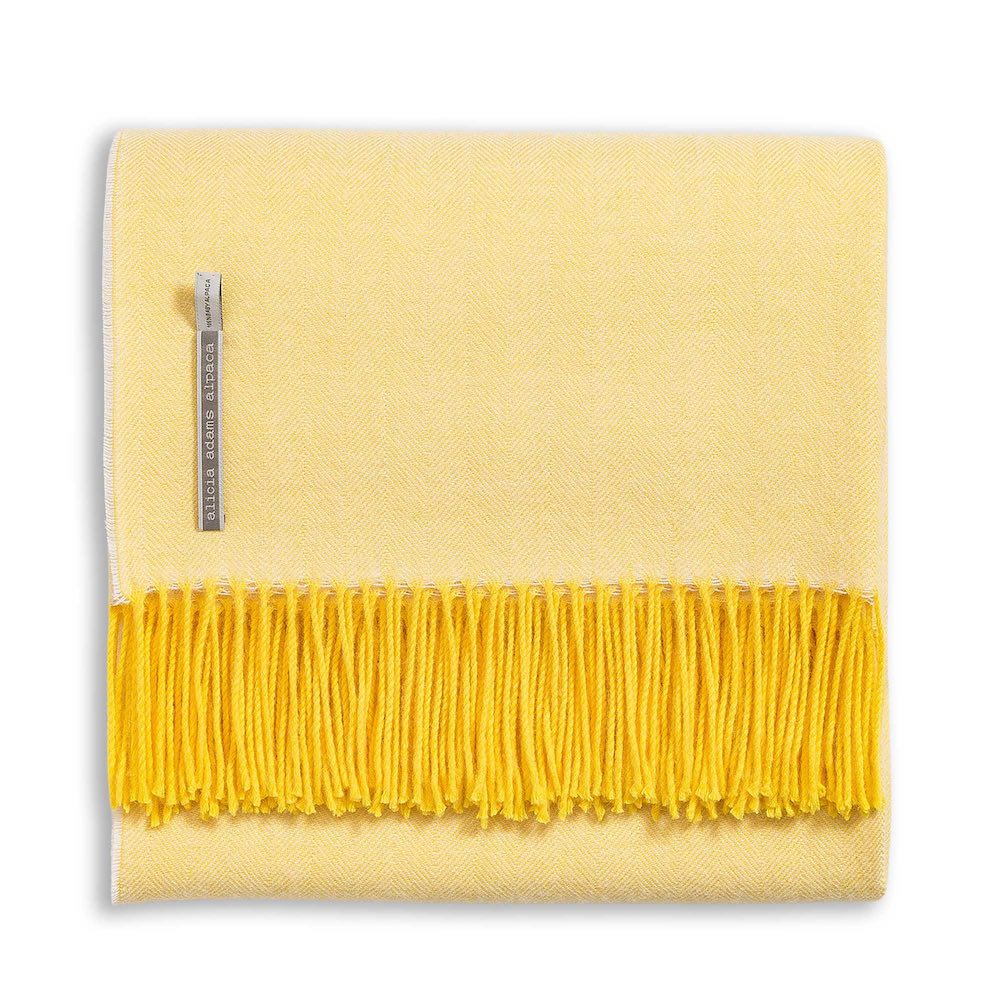 Alicia Adams Alpaca Classic Herringbone Throw: a folded yellow baby alpaca blanket with darker yellow fringe, fair-trade made in Peru, features a herringbone pattern and side fabric tag.