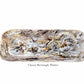The "Mocha Resin Serveware Collection" by Nashi Home features a rectangular platter with a marbled gray, white, and brown design. Food safe and stylish, it’s perfect for home decor or serving guests.