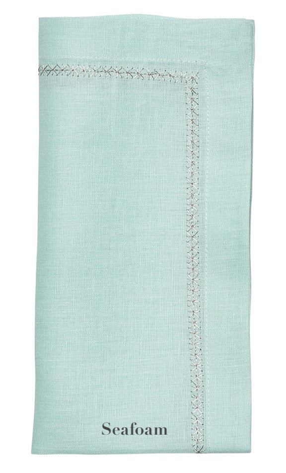 The Kim Seybert Classic Napkin Set features a folded seafoam green linen napkin, highlighted by decorative stitching and an elegantly embroidered border.