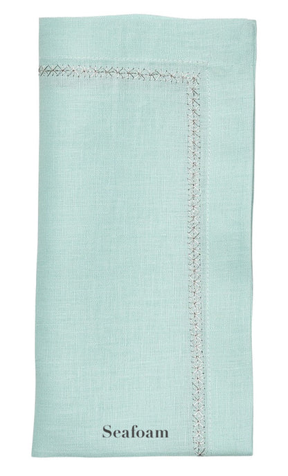 The Kim Seybert Classic Napkin Set features a folded seafoam green linen napkin, highlighted by decorative stitching and an elegantly embroidered border.