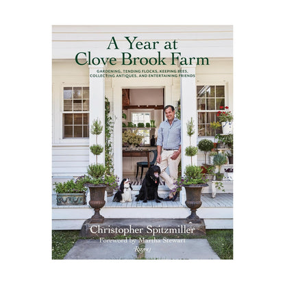 A man stands on a porch with two dogs, surrounded by potted plants at Clove Brook Farm. The book “A Year at Clove Brook Farm” by Common Ground captures the charm of this idyllic country retreat.