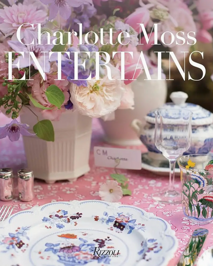 A beautifully arranged floral tablescape featuring Rizzoli china, a teacup, elegant glassware, and a lush flower arrangement creates an inviting setting for entertaining. The title “Charlotte Moss Entertains” is prominently displayed at the top.