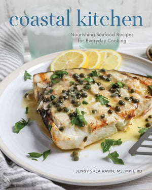 A plate of cooked fish garnished with capers, parsley, and lemon slices sits beneath the title “Coastal Kitchen” from Simon & Schuster, inviting you to discover nourishing seafood recipes inspired by the fresh flavors of coastal living.