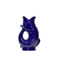 The Original Gluggle Jug’s Fish Gluggle Jug Collection features a glossy, deep blue fish-shaped jug with an open mouth and a handle formed by its curved tail—a British design icon.