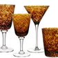 Four amber and brown patterned glassware pieces from the William Yeoward Crystal Vanessa Tortoise Collection—two wine glasses, a martini glass, and a tumbler—are arranged on a white background for an optical illusion effect.