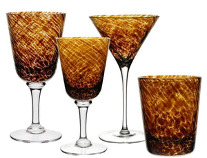 Four amber and brown patterned glassware pieces from the William Yeoward Crystal Vanessa Tortoise Collection—two wine glasses, a martini glass, and a tumbler—are arranged on a white background for an optical illusion effect.