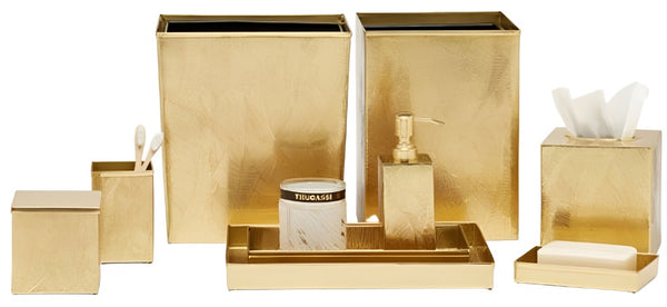 The Pigeon & Poodle Mancora Collection features gold-plated bathroom accessories including trash cans, a toothbrush holder, a candle, a soap dispenser, tissue box, and a soap tray. Each piece exudes golden hour hues and is arranged neatly on a white background.