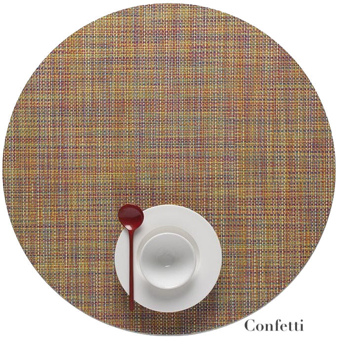 The Chilewich Round Placemat displays a multicolored Mini Basketweave pattern, crafted from phthalate-free Terrastrand yarns. A white cup, saucer, and red spoon rest on top, with "Confetti" text shown in the corner.