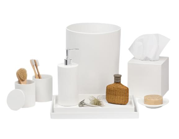 The Cordoba Bath Collection by Pigeon & Poodle features white ceramic accessories—soap dispenser, toothbrush holder, brush, cup, tissue box, tray, soap dish, decorative bottle, and plant—displayed on a subtly textured white surface.
