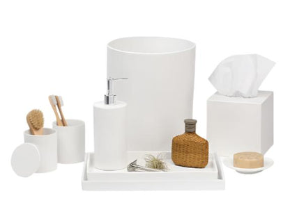 The Cordoba Bath Collection by Pigeon & Poodle features white ceramic accessories—soap dispenser, toothbrush holder, brush, cup, tissue box, tray, soap dish, decorative bottle, and plant—displayed on a subtly textured white surface.
