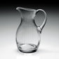The William Yeoward Crystal Corinne Pitcher, tall and clear with vertical ridges and a curved handle, from the Corinne Collection is displayed on a gray gradient background.