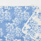 This blue and white floral towel from the Weezie Towels x Meg Braff Bath Collection has a classic white border and is partially folded at one corner.