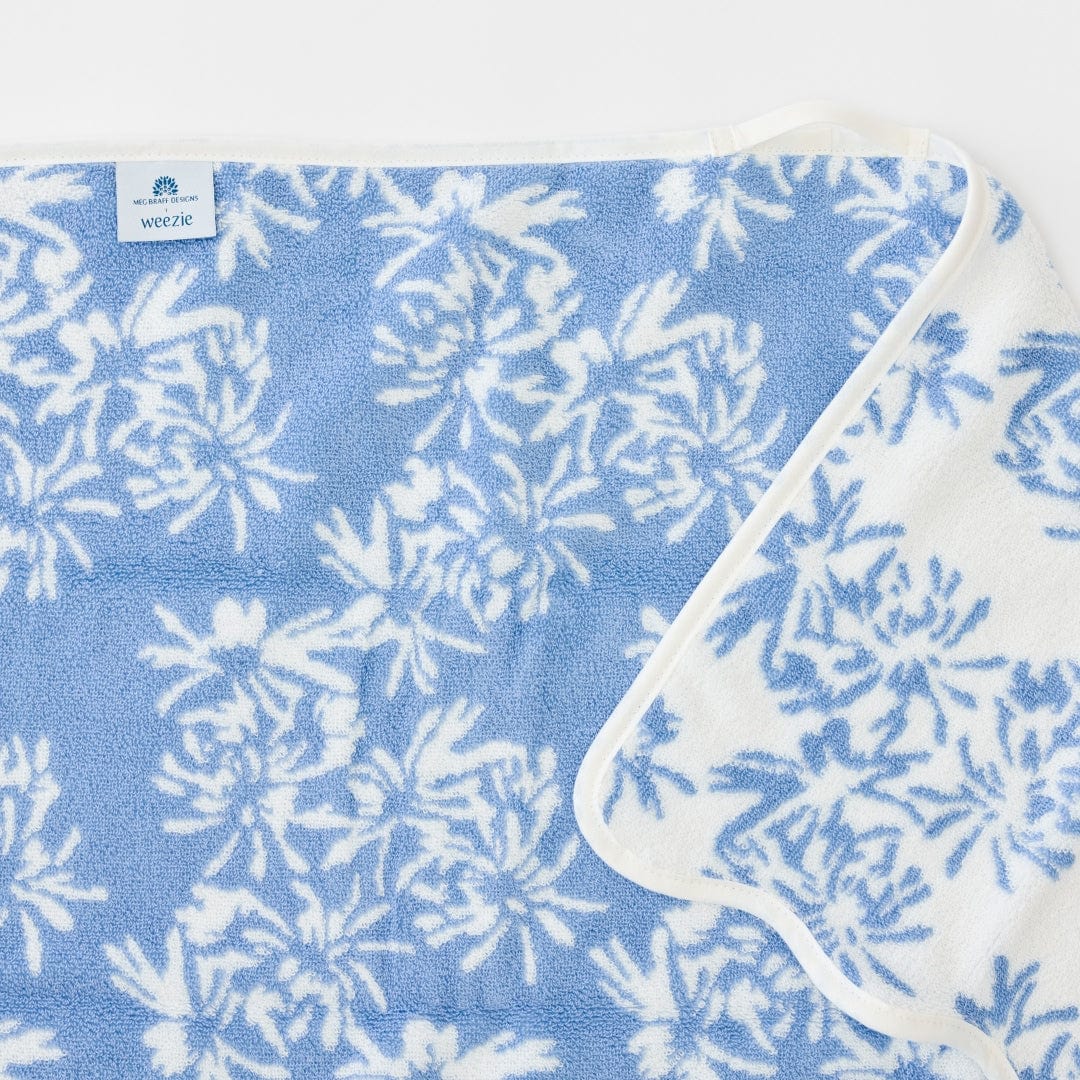 This blue and white floral towel from the Weezie Towels x Meg Braff Bath Collection has a classic white border and is partially folded at one corner.