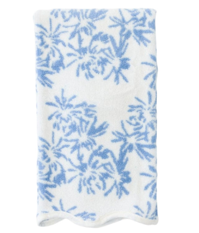 The Weezie Towels x Meg Braff Bath Collection showcases a folded white towel with a light blue floral pattern and scallop trim, capturing Palm Beach's breezy charm.