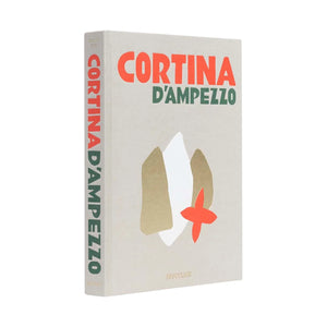 The hardcover book "Cortina d'Ampezzo" by Assouline features bold red and green text with abstract shapes on a beige cover and celebrates the breathtaking Dolomites in Italy’s Alps.