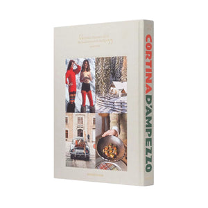The Assouline "Cortina d'Ampezzo" book stands upright against a white background, its cover featuring a collage of winter and food images that reflect the lively spirit of the Italian Alps and the beauty of the Dolomites.
