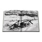 An open Assouline "Cortina d'Ampezzo" book shows a black-and-white photo of four people sledding on snowy hills near a mountain village, with the Dolomites rising in the background.